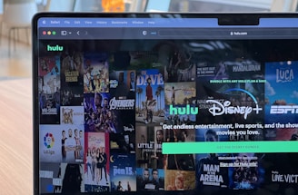 A laptop screen displays a web page featuring a mix of movie and TV show covers, highlighting popular titles and a Hulu and Disney+ bundle promotion. There are visible icons and images of films and shows alongside promotional text offering entertainment and live sports.